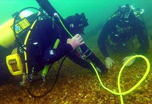 two divers in full SCUBA gear preparing to airlift an artefact