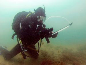 diver in full SCUBA gear holding a clipboard underwater