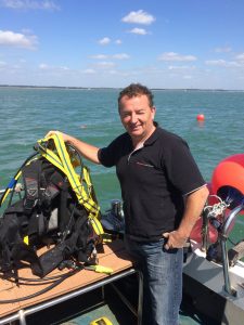 diver standing with SCUBA kit in front of the ocean