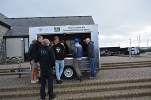 several people standing outside the MSDS marine outreach trailer. the window of the trailer is open and inside you can see informative posters.