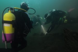 three divers underwater investigating a shipwreck as part of the Y heritage make a splash project.