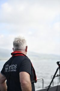 a man in an MSDS Marine branded t-shirt is facing away from a camera and looking towards the ocean.