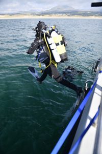 a diver in full SCUBA gear is leaping off the side of a boat into water.