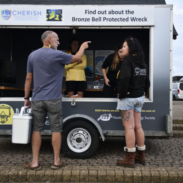 two people are standing outside and two people are standing within the MSDS Marine outreach trailer.