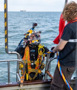 a diver in full SCUBA gear going down the boat ladder into the ocean