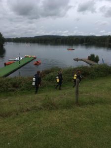 three divers in wetsuits and carrying oxygen tanks walk down a hill towards a small dock in a lake. the kit was funded by the MSDS marine student award.