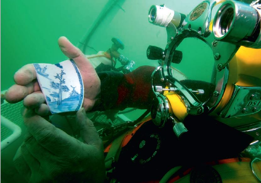 A diver holding a piece of blue and white pottery underwater.